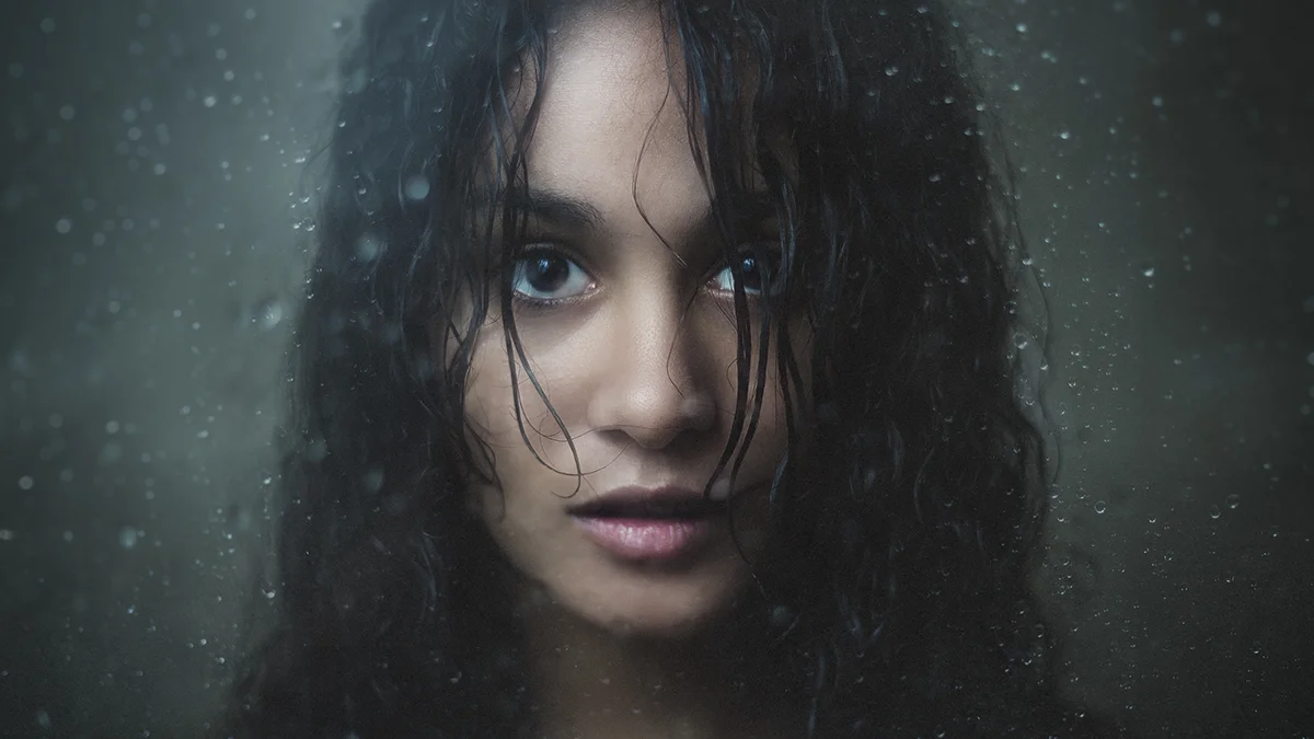 A beautiful woman behind wet foggy glass